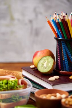 Okul öğle yemeği molası ile sağlıklı öğle yemeği kutusu ve okul malzemeleri ahşap masa, seçici odak kavramı.