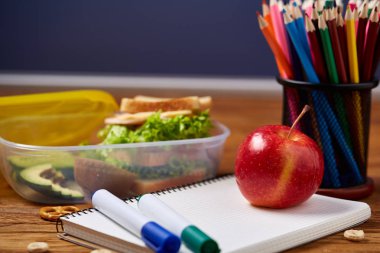 Okul öğle yemeği molası ile sağlıklı öğle yemeği kutusu ve okul malzemeleri ahşap masa, seçici odak kavramı.