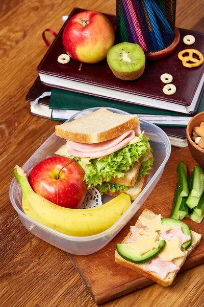 Okul öğle yemeği molası ile sağlıklı öğle yemeği kutusu ve okul malzemeleri ahşap masa, seçici odak kavramı.