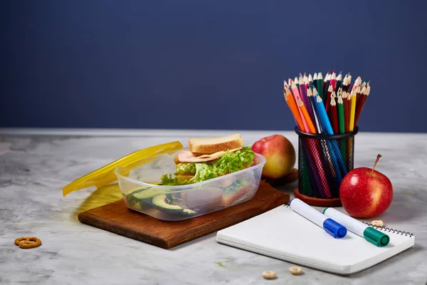 Okul öğle yemeği molası ile sağlıklı öğle yemeği kutusu ve okul malzemeleri ahşap masa, seçici odak kavramı.