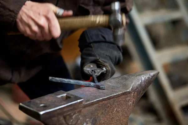 Close-up van een smeden handen manipuleren van een metalen stuk boven zijn smederij, selectieve aandacht. — Stockfoto