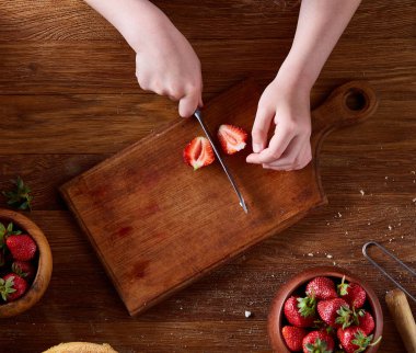 Ahşap masa, üstten görünüm, selctive odak taze çilek kesme kız elinde bıçak.