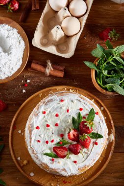 Çilekli tart ahşap arka plan üzerinde düz yatıyordu organik maddeler tarafından çevrili ekşi krem şanti ile kaplı.