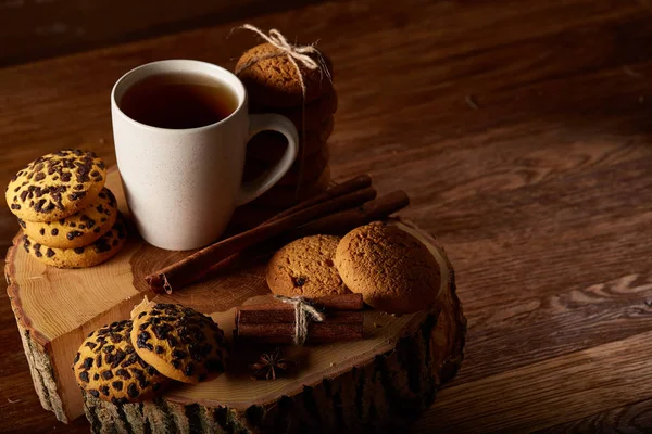 Taza blanca de té y galletas en un registro sobre fondo de madera estilo país, primer plano, enfoque selectivo —  Fotos de Stock