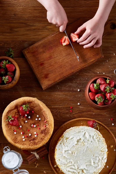 Ahşap masa, üstten görünüm, selctive odak taze çilek kesme kız elinde bıçak.