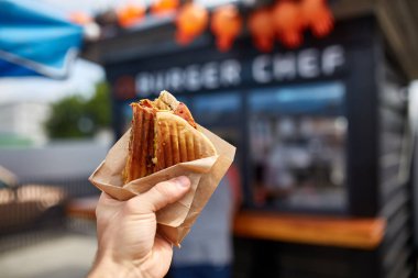 İlk kişi görünümü atış bir adam yeme hamburger sokak kafe, yumuşak odak, sığ derinlik-in tarla.