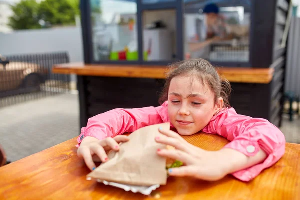 Menina bonito vai comer um hambúrguer de queijo no café ao ar livre — Fotografia de Stock