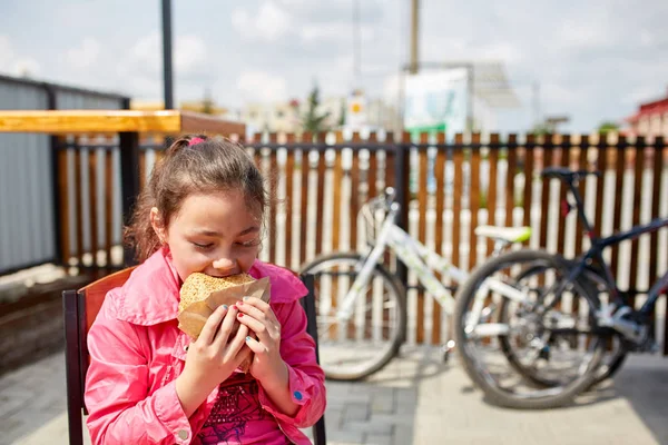 Девушка ест чизбургер в кафе под открытым небом перед стоянкой велосипедов . — стоковое фото