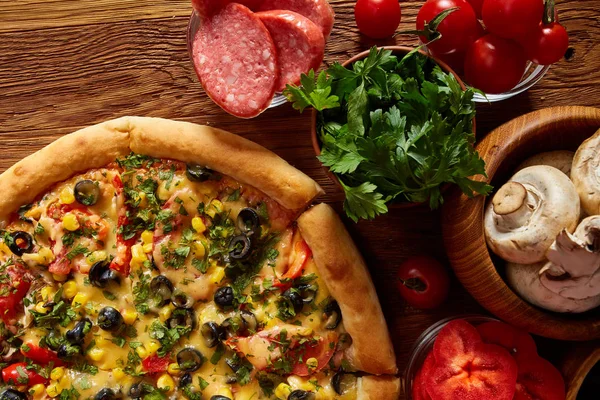 Pizza natürmort. Taze pişmiş pizza ve bileşenlerinin ahşap arka plan üzerine düzenlenmiş bir parçası.