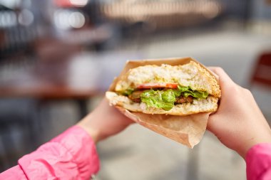 İlk kişi sokak kafe, yumuşak odak, sığ derinlik-in tarla hamburger yeme bir kız görüntüsünü göster.