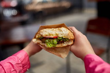 İlk kişi sokak kafe, yumuşak odak, sığ derinlik-in tarla hamburger yeme bir kız görüntüsünü göster.