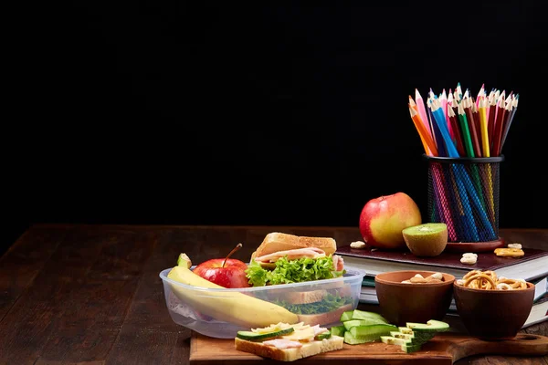 Okul öğle yemeği molası ile sağlıklı öğle yemeği kutusu ve okul malzemeleri ahşap masa, seçici odak kavramı.
