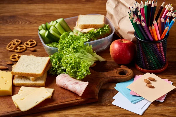 Okul öğle yemeği molası ile sağlıklı öğle yemeği kutusu ve okul malzemeleri ahşap masa, seçici odak kavramı.