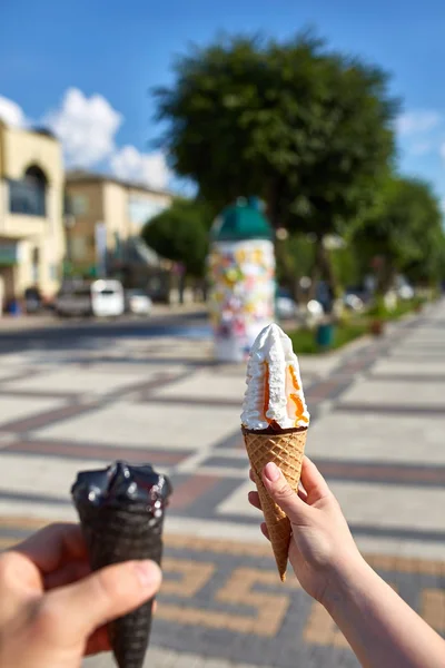 A first person view, female walking along the road with an ice cream in her hands, shallow depth of field.