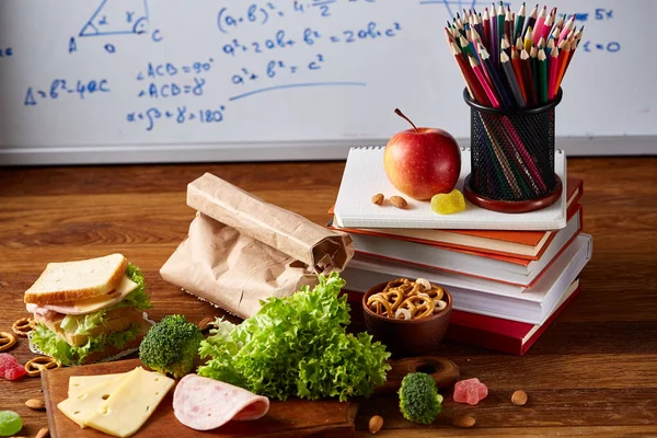 Okul öğle yemeği molası ile sağlıklı öğle yemeği kutusu ve okul malzemeleri ahşap masa, seçici odak kavramı.