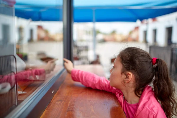 Nyfiken liten flicka väntar hennes burger i gatan skyltfönstret. — Stockfoto