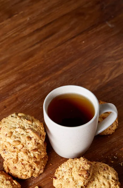 Caneca de porcelana branca de chá e biscoitos doces em pedaço de madeira sobre fundo de madeira, vista superior, foco seletivo — Fotografia de Stock