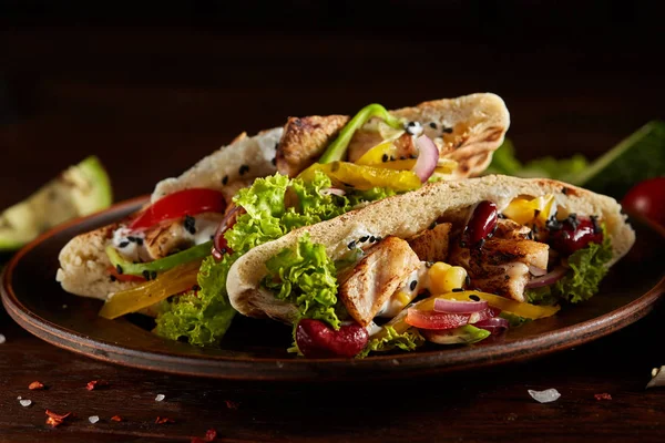 stock image Pita stuffed with chicken, beans and letucce on clay plate over wooden background, side view, selective focus.