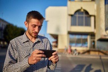 Kentsel ortamda duran cep telefon kullanarak rahat kıyafetler içinde sakallı erkek portresi yarım uzunluk.
