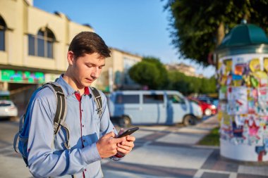 Şehirde yer Park yeri arka plan üzerinde yürüyüş onun elinde bir akıllı telefon ile gülümseyen genç bir adam