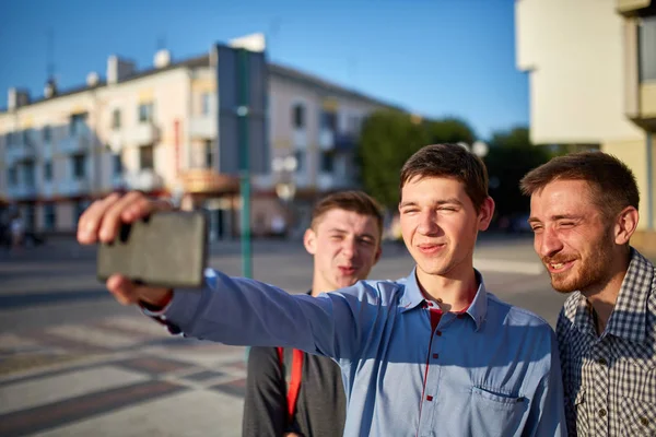 Retrato de un grupo de amigos sonrientes y sonrientes en vacaciones de verano, haciendo selfie en cámara sobre fondo urbano . — Foto de Stock