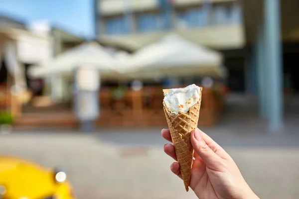 A first person view, a person walking along the road with an ice cream in her hands, shallow depth of field.