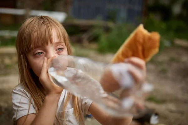 Retrato de pobre sem-teto menina água potável de garrafa de plástico no beco sujo — Fotografia de Stock