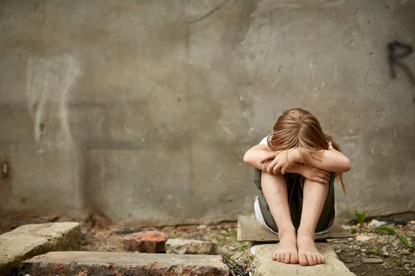 Street photo of girl orphan with holen knees under the dirty city wall. — Stock Photo, Image