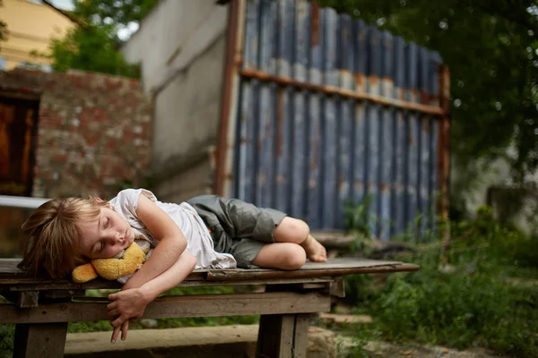 Unglückliches Streunerkind liegt auf dem Brett in der schmutzigen Gasse, geringe Schärfentiefe. — Stockfoto