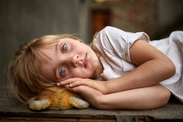 Portrét nešťastných zbloudilé dítě ležící na palubě v špinavé uličce, malá hloubka ostrosti. — Stock fotografie