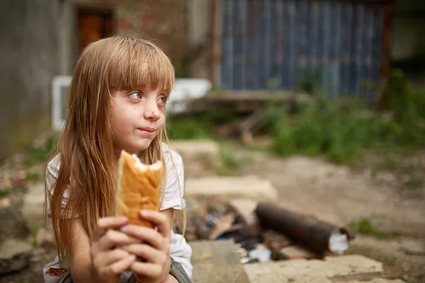 Portret van hongerige dakloos meisje eten een stukje brood in het vuile steegje Rechtenvrije Stockfoto's