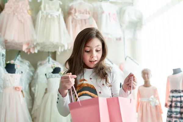 Linda niña en las compras. retrato de un niño con bolsas de compras. niño en vestido, gafas de sol y zapatos cerca del centro comercial que se divierten. compras Imagen De Stock