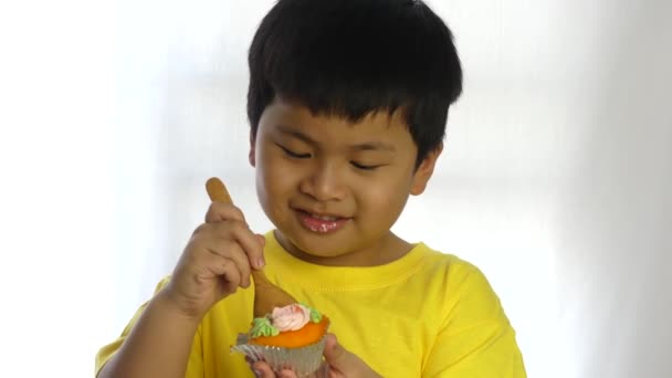 アジアのかわいい小さな男の子が白い背景で木のスプーンでケーキを食べる — ストック動画