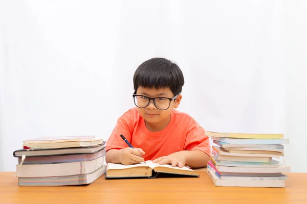 Söt en liten pojke skriver en bok på bordet med på vit rygg — Stockfoto