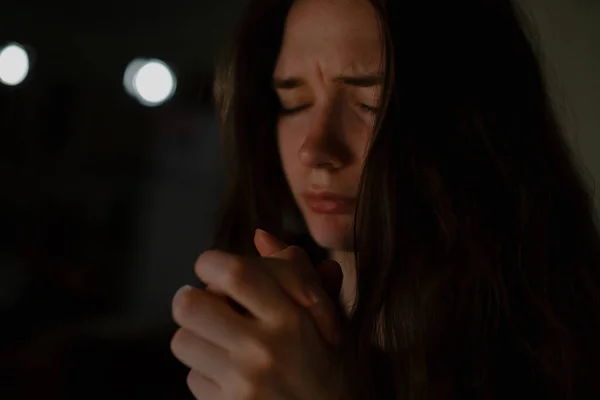 Young woman prays to God in the apartment at night, close-up.