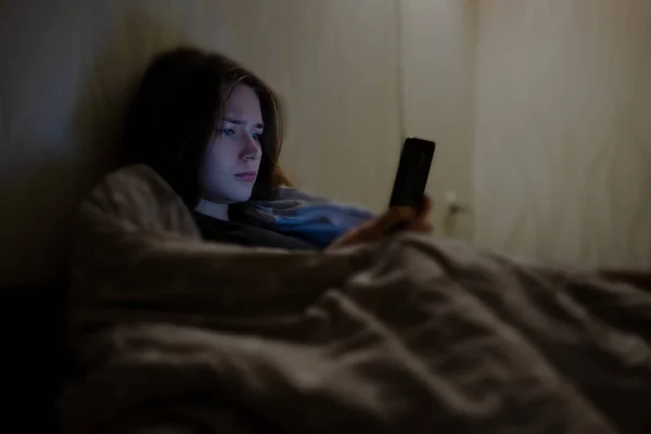 Gece yatakta akıllı telefon kullanan bir kadın.