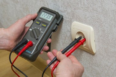 Bir elektrikçi aparatı kullanarak voltajdaki voltajı ölçer.