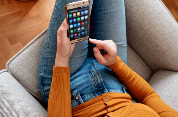 Yukardan genç bir kadının ev sarısı turuncu renkte akıllı telefon kullanması.
