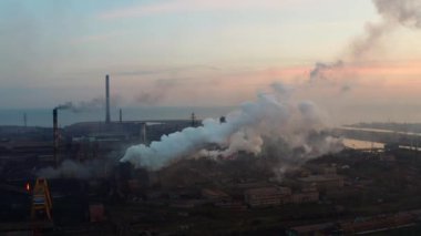 Borular gökyüzüne karşı endüstriyel işletmenin üzerinden günbatımında duman. Arka planda deniz görebilirsiniz. Havadan çekim
