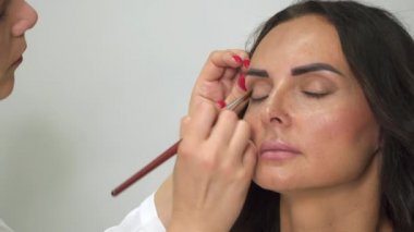 Bir fırça ile profesyonel makyaj sanatçısı bir kadının yüzüne bir gölge koyar.