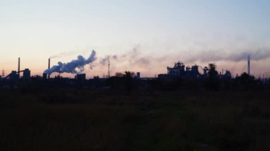 Şafakta gökyüzüne karşı metalürjik bir bitkinin bacalarından duman