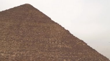 Bulutlu gökyüzünün arka planında Cheops Piramidi. Kuşlar gökyüzünde uçar. Cheops Piramidi, Büyük Giza Piramidi - Mısır piramitlerinin en büyüğü.