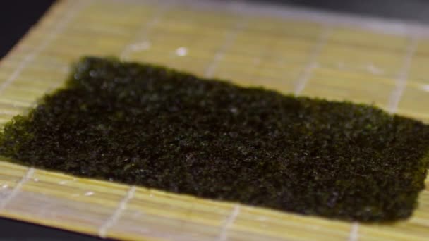 Εξάπλωση μαγειρεμένο ρύζι σε ένα χαρτί φύκια πάνω από ένα ρολό μπαμπού για να κάνει ρολό σούσι — Αρχείο Βίντεο