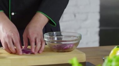 Birisi zeytinyağlı kristal bir kaseye soğan dilimleri atıyor.