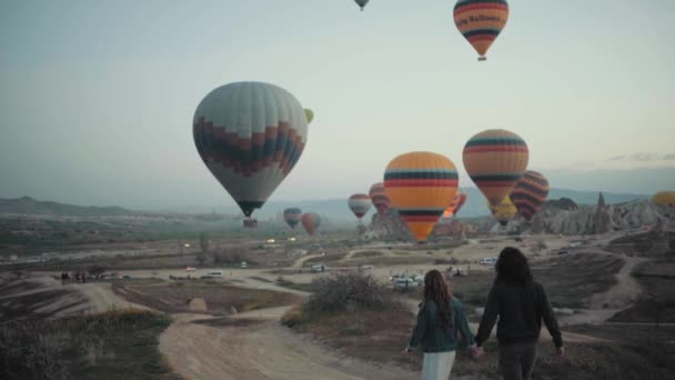 Imágenes en cámara lenta de una pareja caminando de la mano hacia el lugar de despegue de los globos de aire caliente — Vídeo de stock