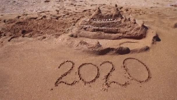 2020 getekend op het zand wordt weggewassen door een golf op het strand — Stockvideo