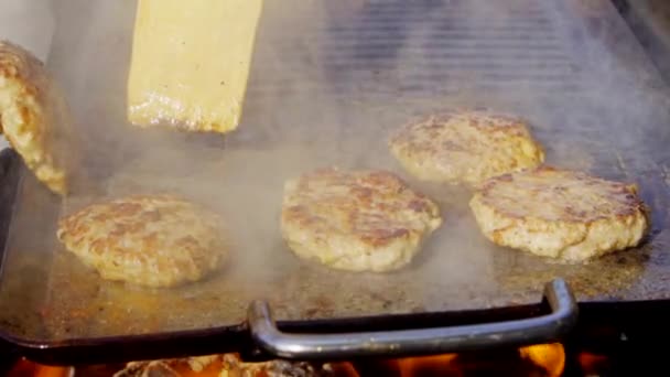 Gros plan des hamburgers de poulet sur le gril avec des flammes de feu, chef les retourne. Mouvement lent — Video