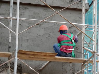 Kuala Lumpur, Malezya-23 Ağustos 2018: çimento alçı kullanarak inşaat işçileri tarafından sıvalı tuğla duvar. İskele geçici evreleme olarak yükseklikte çalışırdım. Kötü olmasını önlemek için uygun güvenlik dişli giyiyor.  