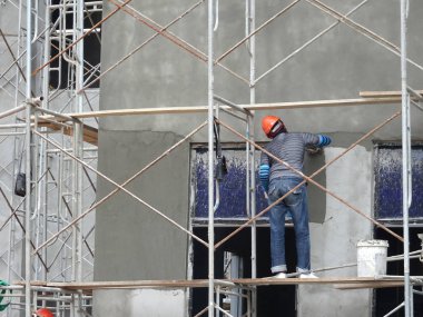 Kuala Lumpur, Malezya-23 Ağustos 2018: çimento alçı kullanarak inşaat işçileri tarafından sıvalı tuğla duvar. İskele geçici evreleme olarak yükseklikte çalışırdım. Kötü olmasını önlemek için uygun güvenlik dişli giyiyor.  