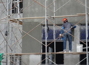 Kuala Lumpur, Malezya-23 Ağustos 2018: çimento alçı kullanarak inşaat işçileri tarafından sıvalı tuğla duvar. İskele geçici evreleme olarak yükseklikte çalışırdım. Kötü olmasını önlemek için uygun güvenlik dişli giyiyor.  